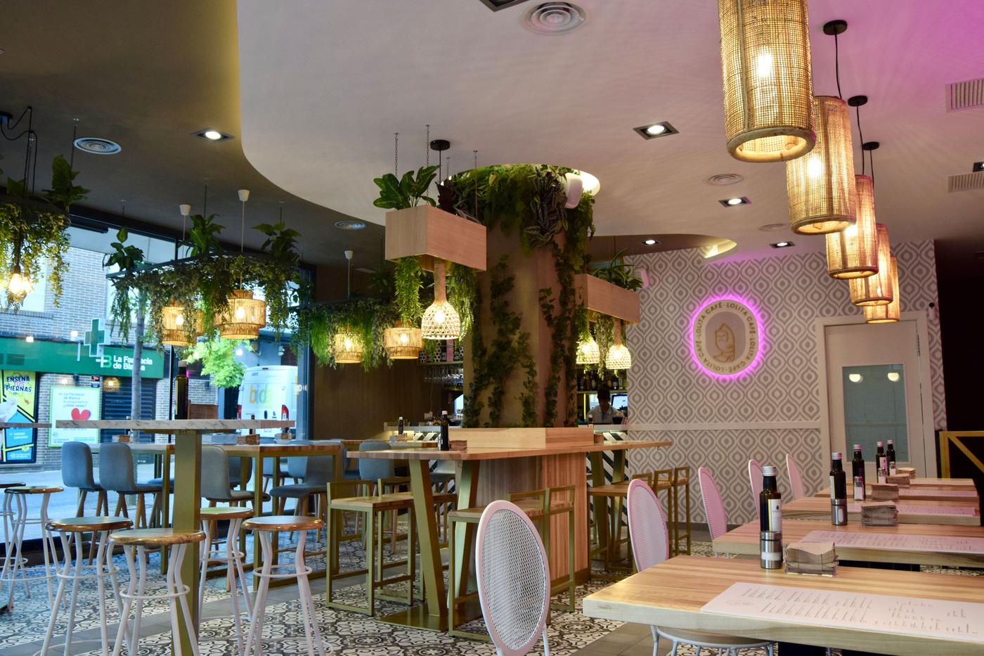 Interior de Lolita Café, con plantas colgantes, mesas de madera y el logo de neón rosa